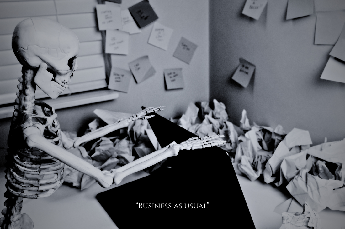 Black-and-white image of a plastic skeleton sitting at a cluttered desk with a laptop, sticky notes, paper stacks, and a pen in hand — a humorous visual metaphor for late-night editing fatigue.
